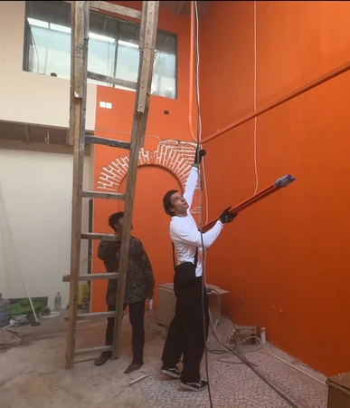Two people painting the boutique wall Mishki orange with a long roller
