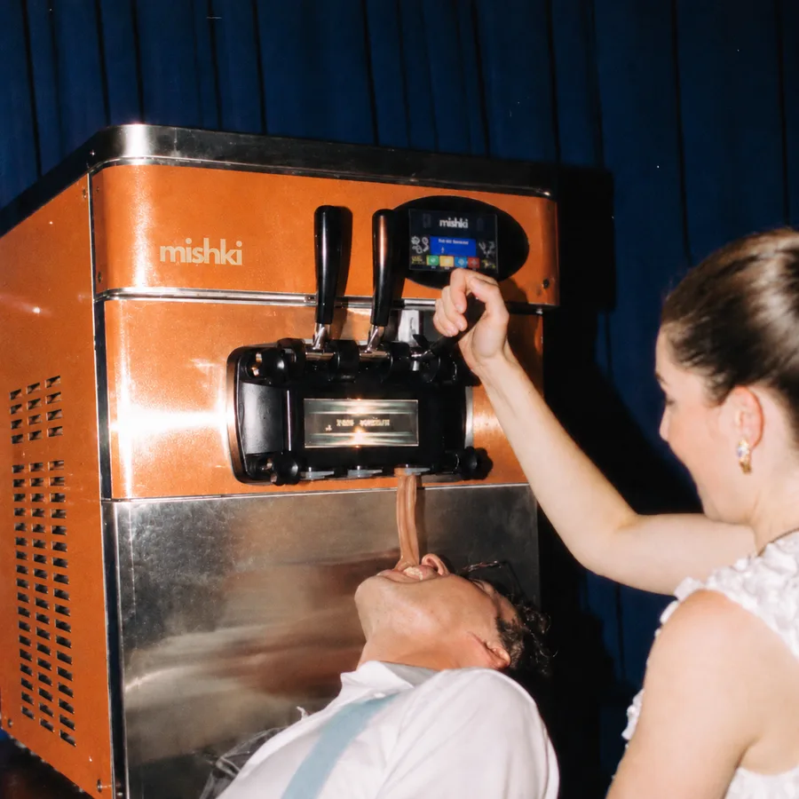 A bride pouring soft-serve from the Mishki machine straight into a guest's mouth