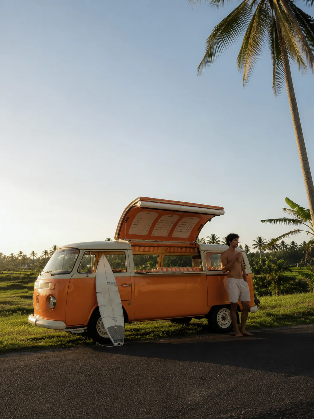 The orange Mishki VW van parked by rice fields with a surfboard leaning on it